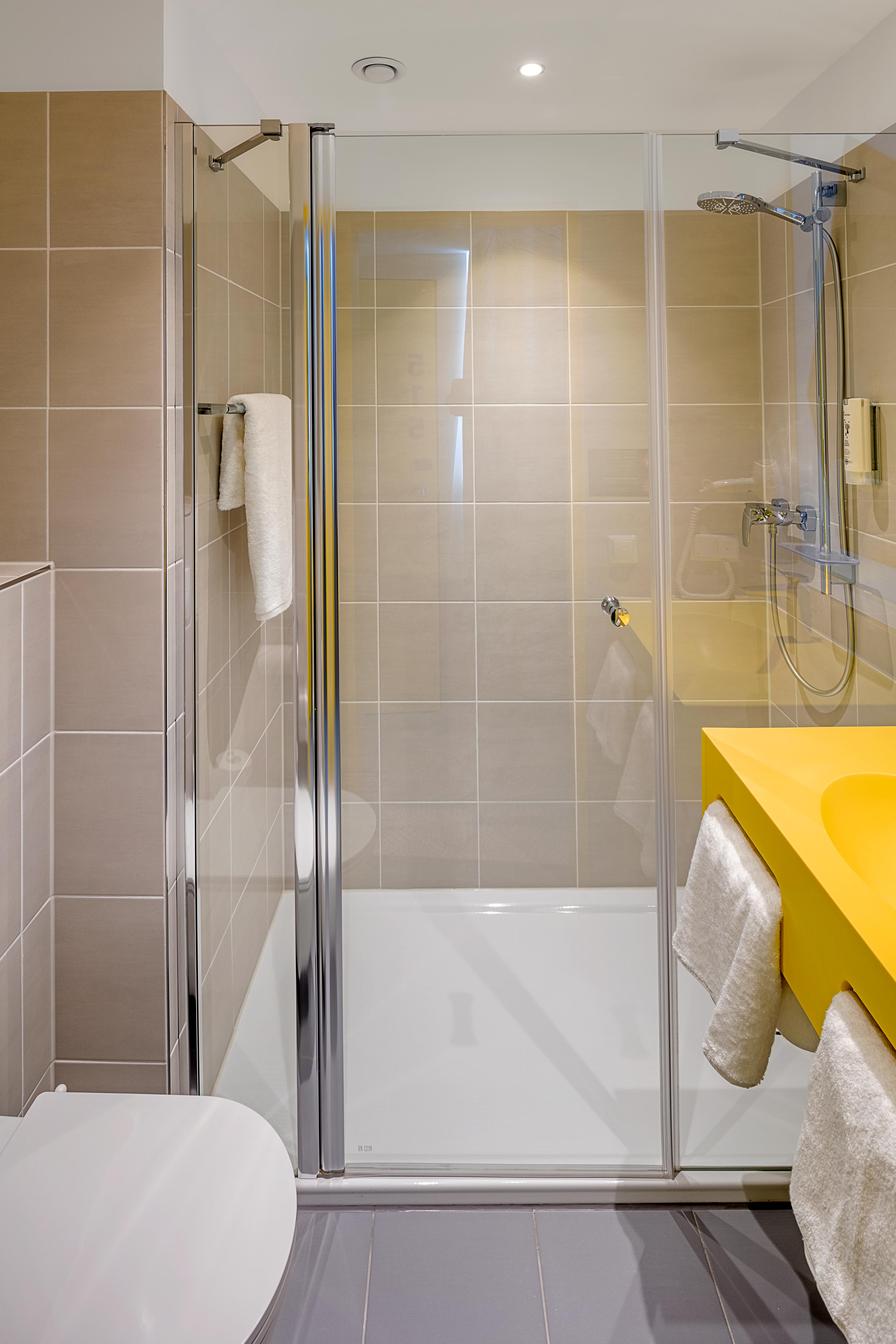 Eine Dusche im Badezimmer des prizeotels, davor ein gelbes Waschbecken