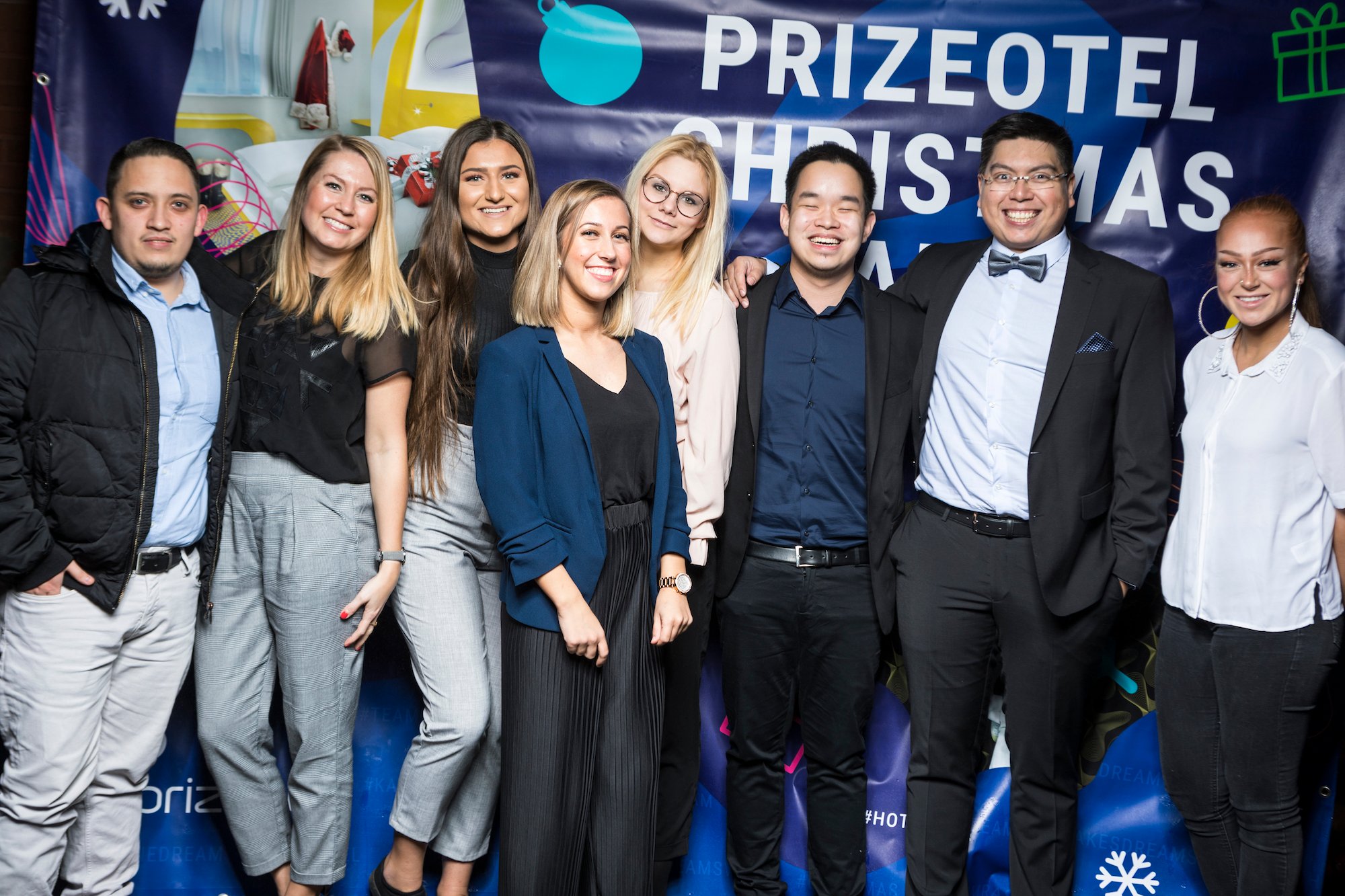 The young team of prizeotel employees is standing in front of a prizeotel poster and smiling