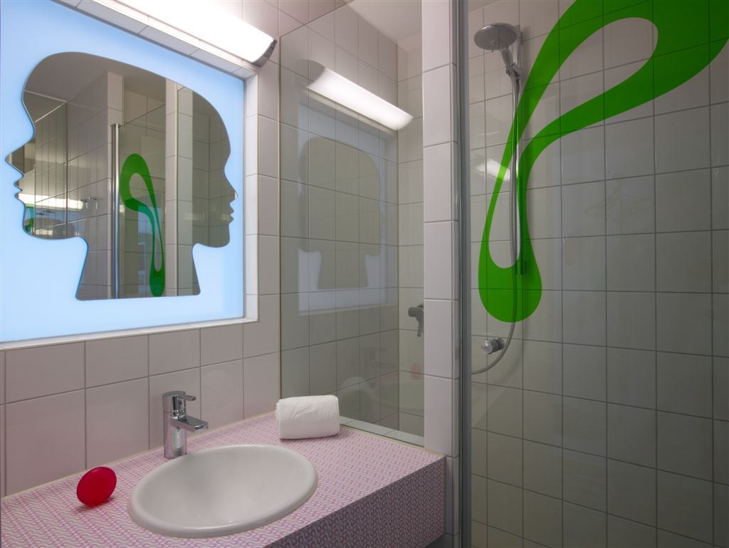 Badezimmer mit Waschbecken und Duschkabine mit aufgedrucktem prizeotel-Logo an der Duschwand