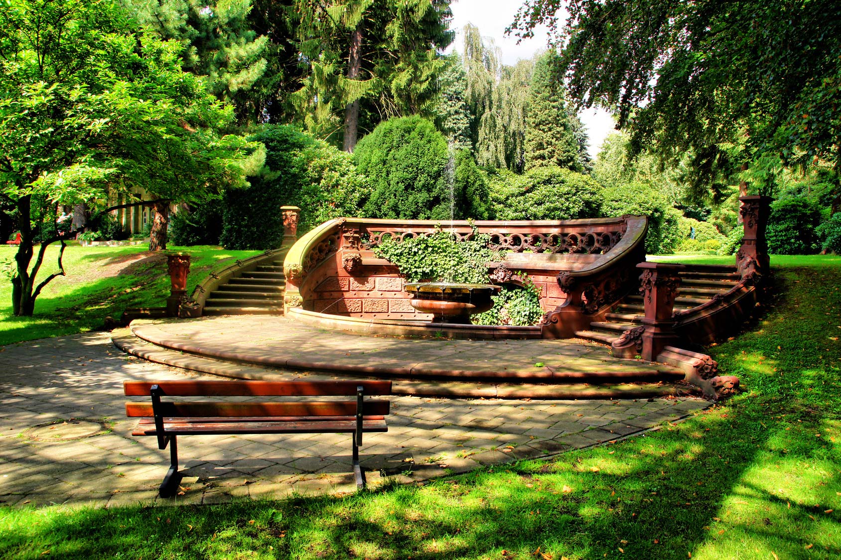 Ein Brunnen und Stufen umgeben von Sitzbänken in einem Park an einem sonnigen Tag
