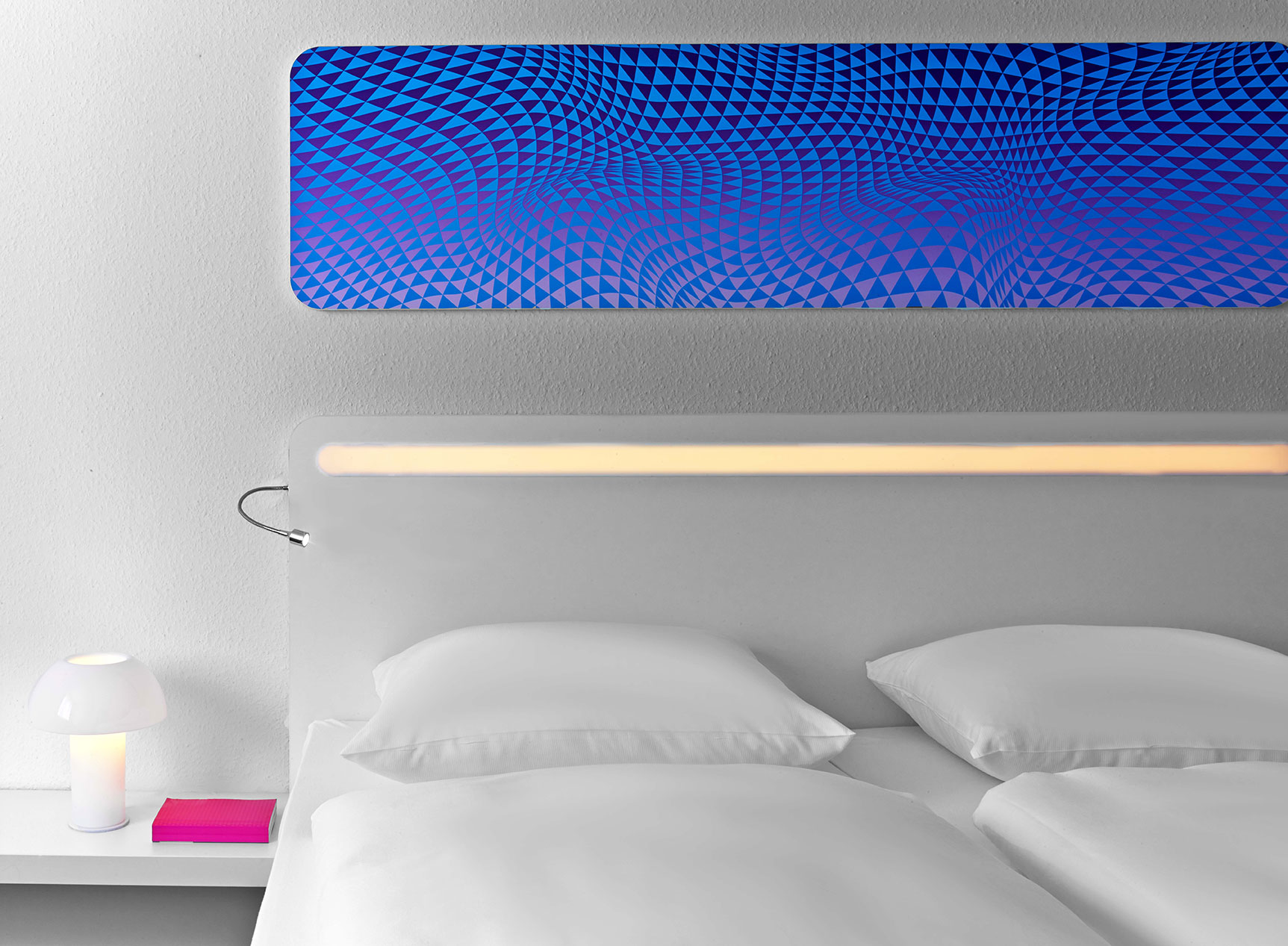 Details of a hotel bed with a reading lamp and a pink book on the nightstand