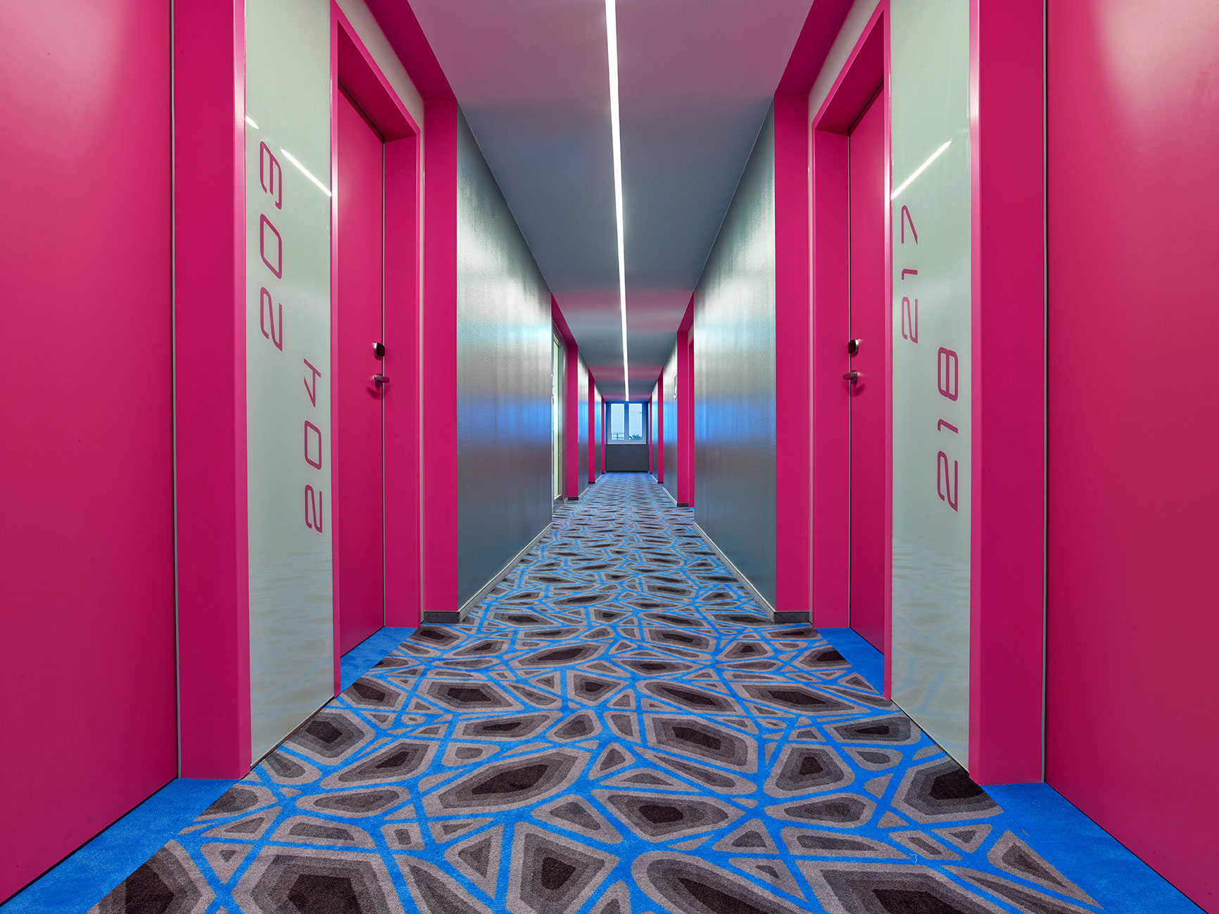 Flur des Hotels mit pinken Wänden und Türen, sowie einem blau gemustertem Boden