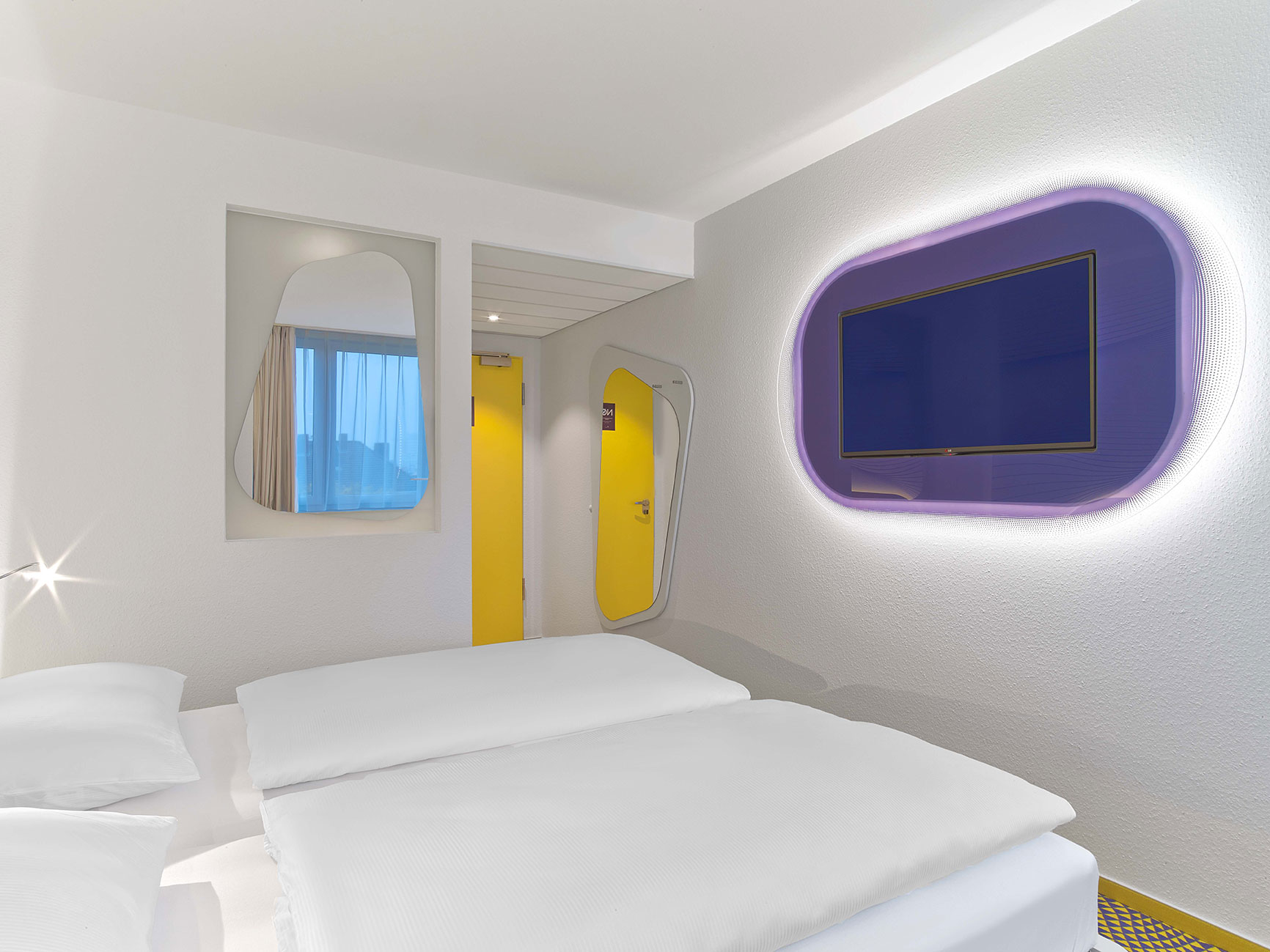Design hotel room with a double bad, a TV and a curved mirror