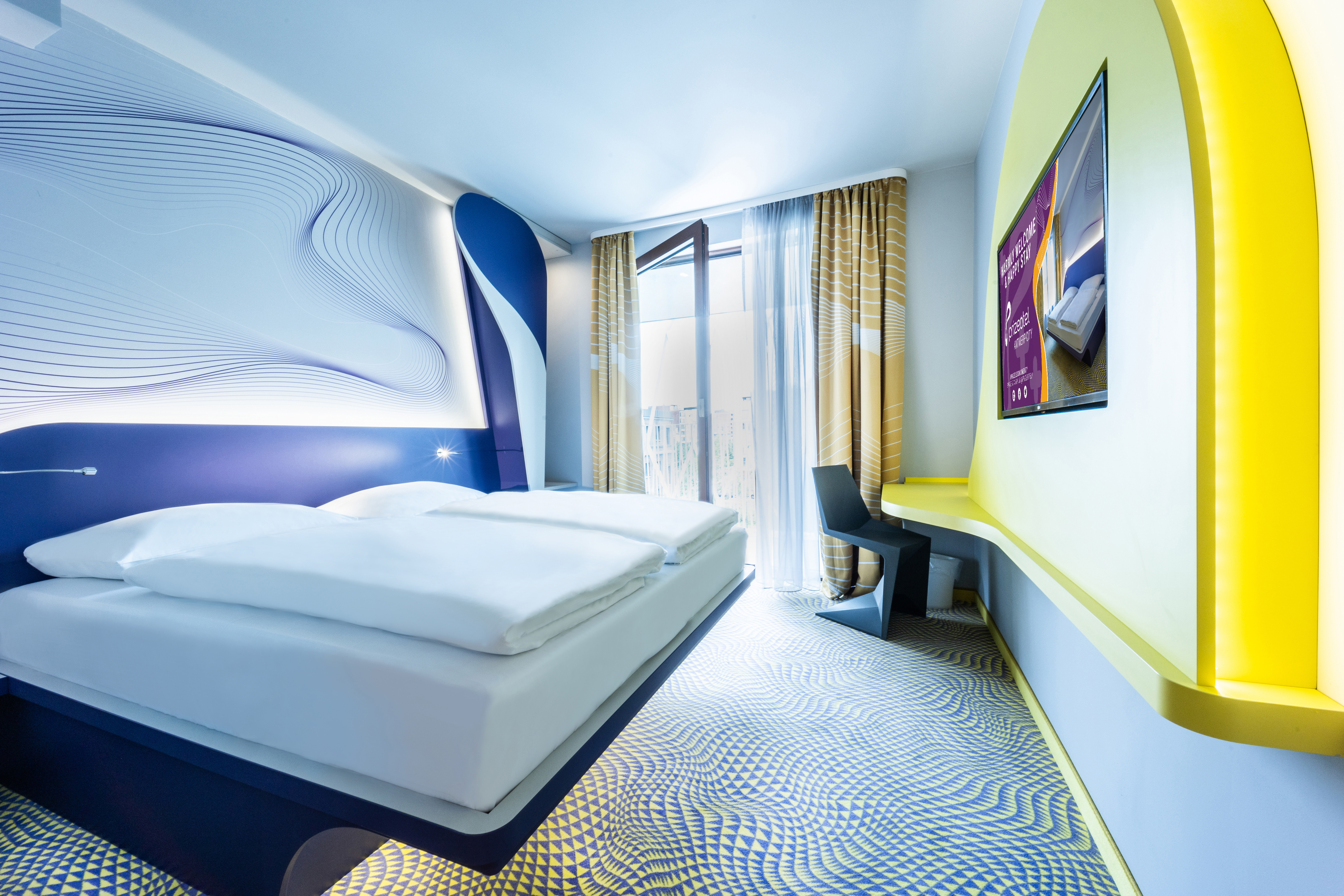 Ein weitläufiges Hotelzimmer gestaltet in blau und gelb mit einem großen Fenster