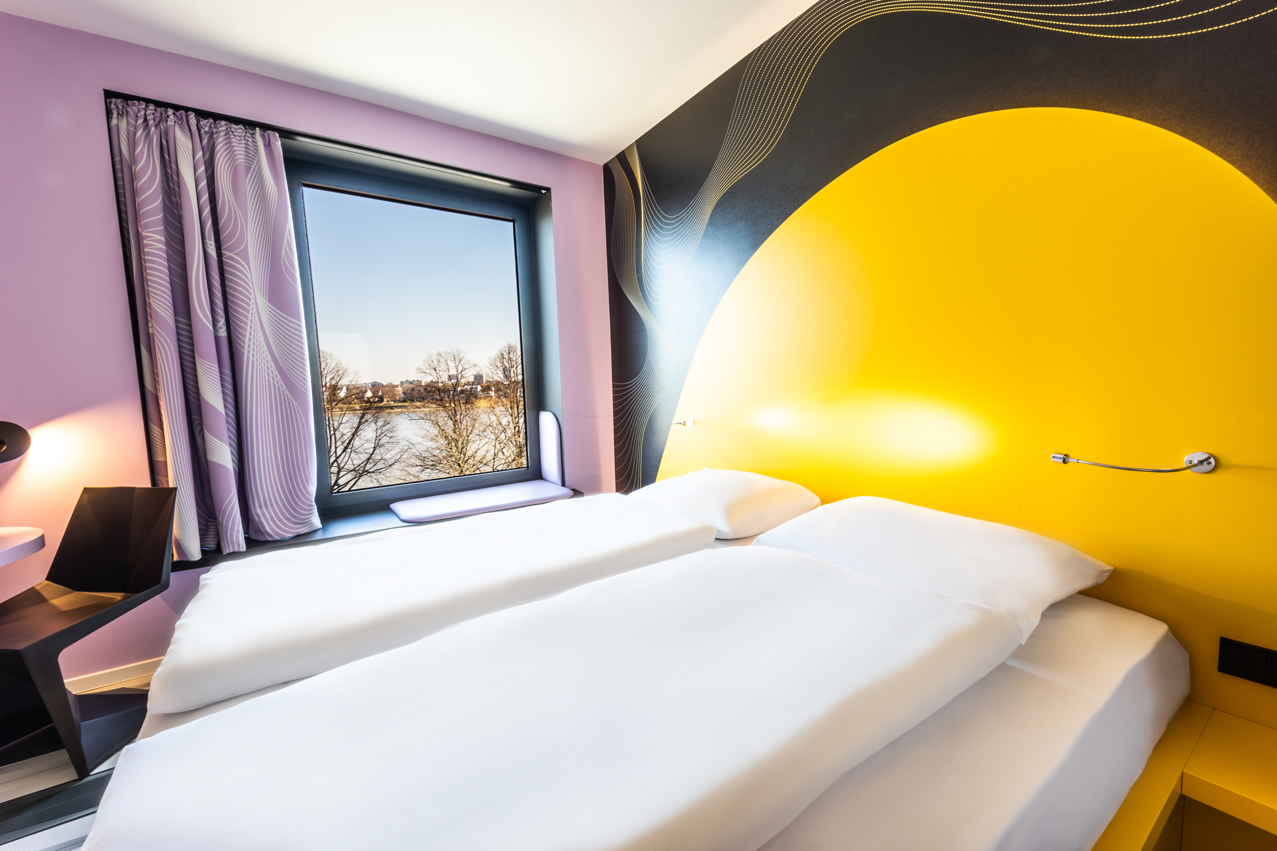 Heller Raum mit gelben Doppelbett und lila Wand