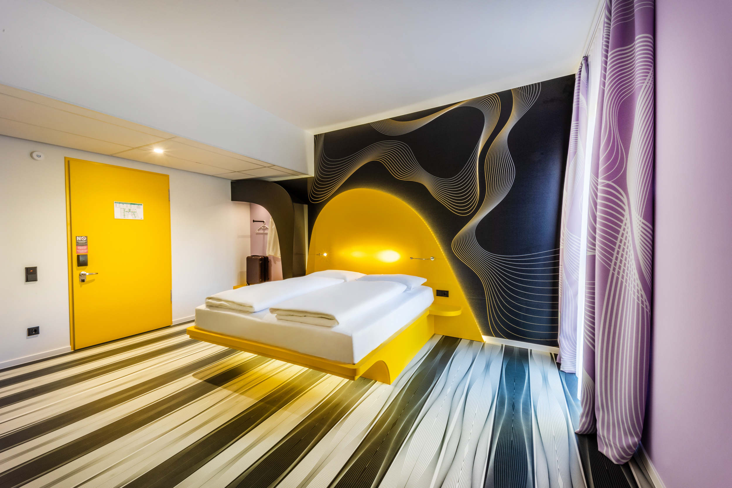 Einblick in ein modernes Hotelzimmer mit gelbem Bett und lila Vorhängen