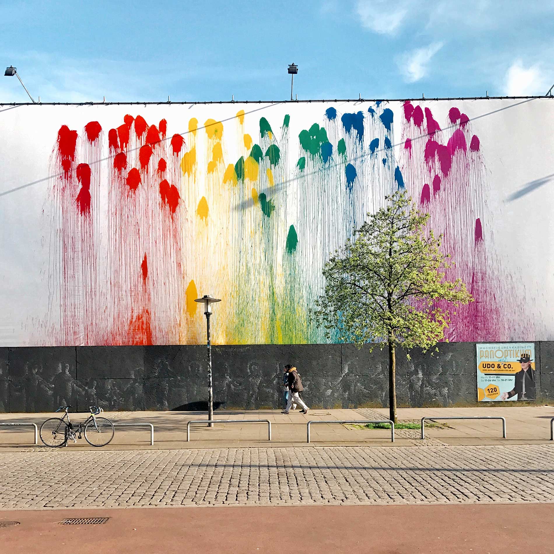 Große weiße Mauer mit binten Farbflecken in Hamburg hinter vorbeigehenden Passanten