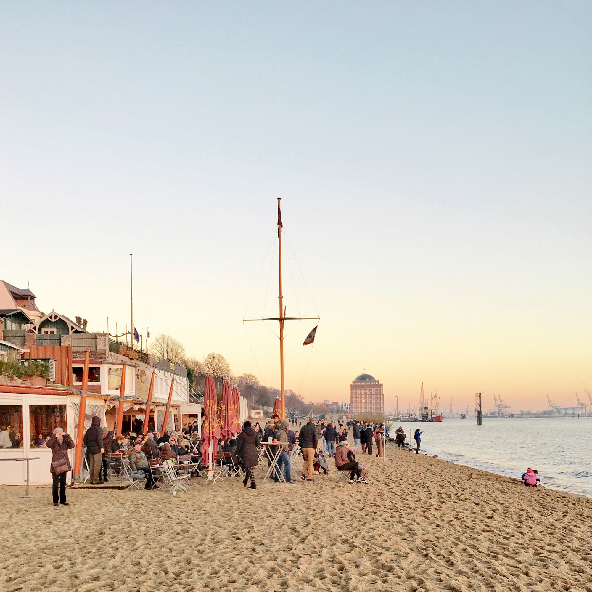 Ein belebter Strand mit bei Sonnenuntergang mit vielen Gästen an einer Strandbar