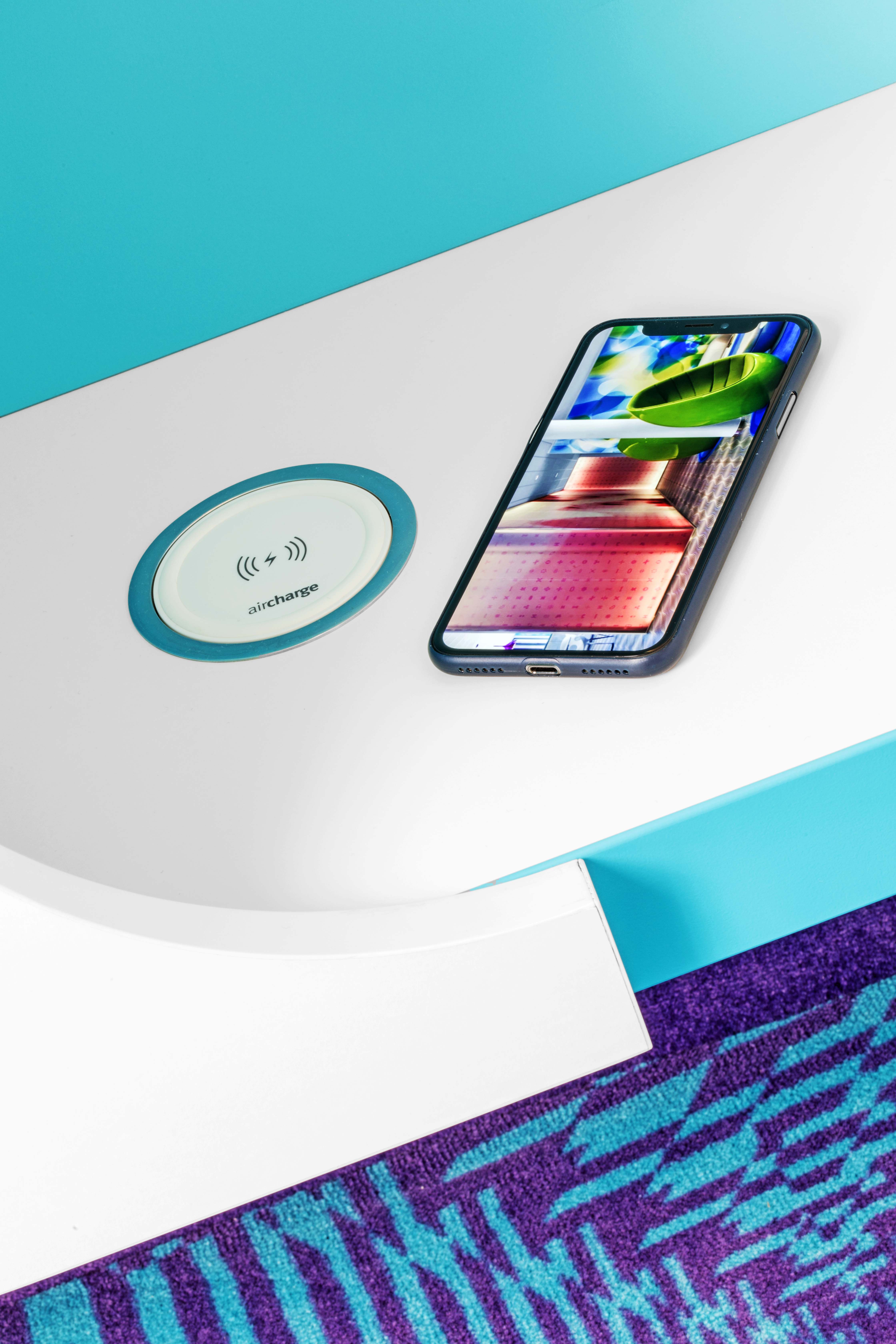 A smartphone is charging on a wireless charging station on a blue table