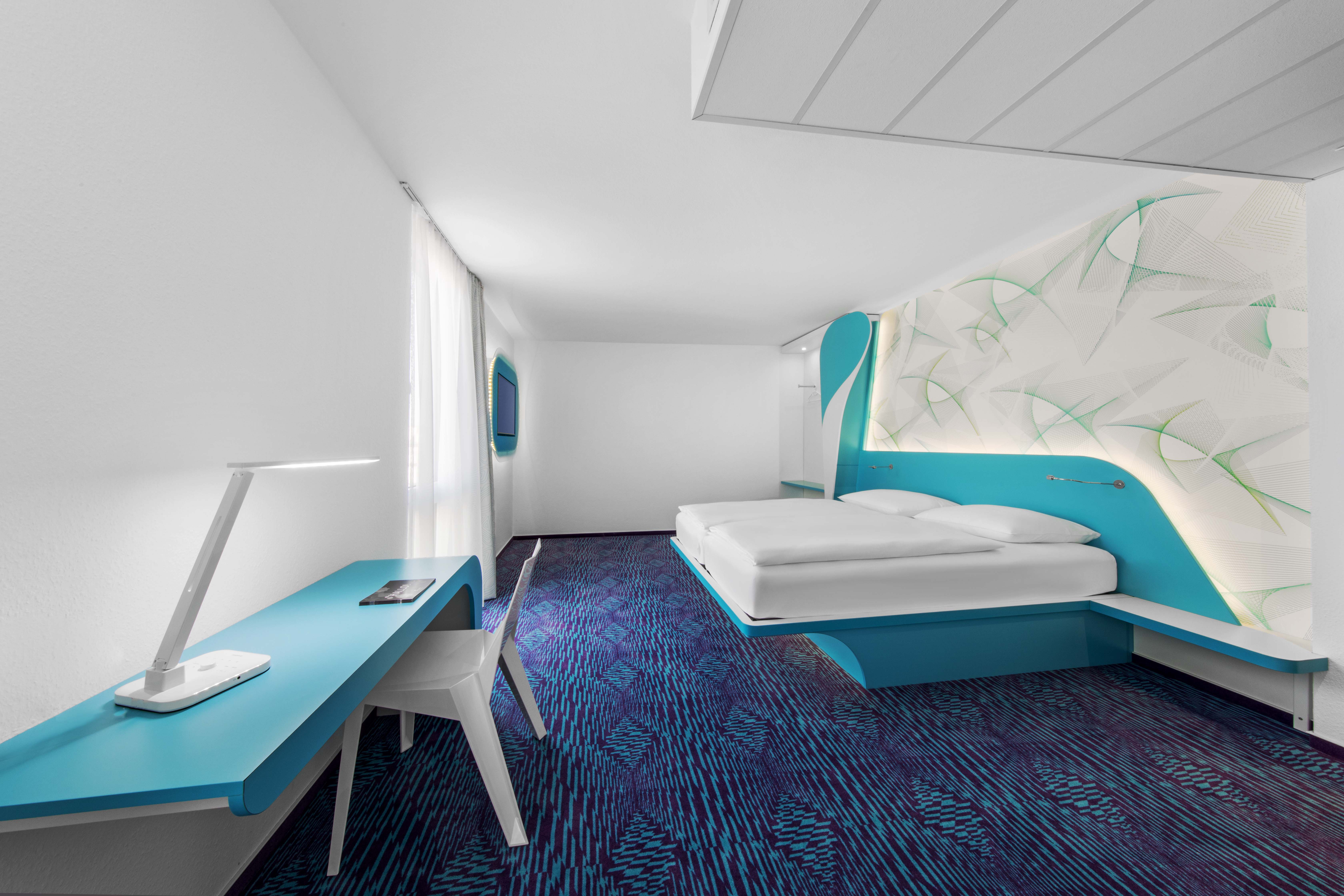 Großes Doppelzimmer des Designhotels in St. Pauli mit blauem Fußboden, kleiner Schreibtischecke und Fernseher