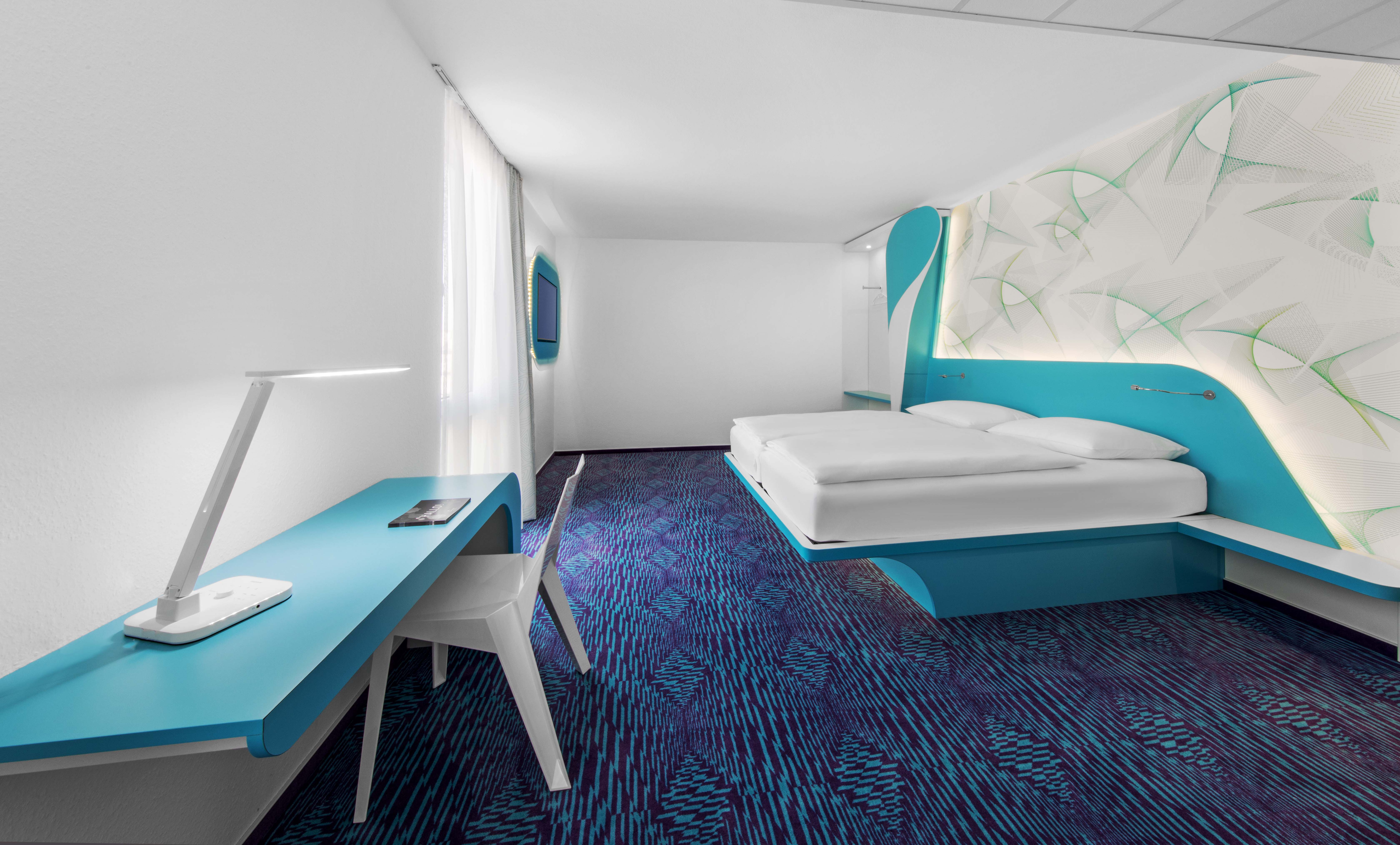 Blau eingerichtetes Hotelzimmer mit Bett, Schreibtisch und Fernseher 