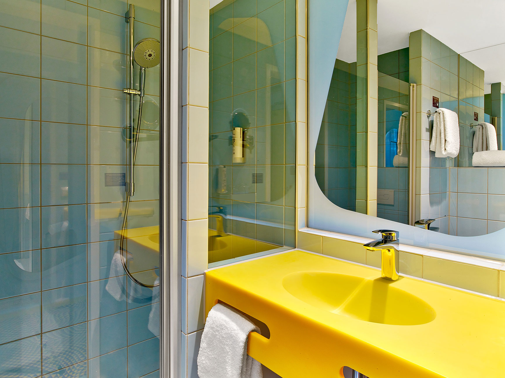 Hotel bathroom with a yellow sink, a shower cabin and blue tiles