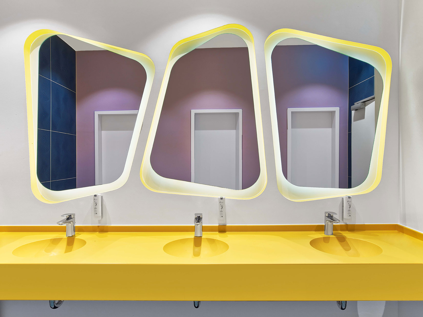 Public bathroom at prizeotel Hanover-City with three curved mirrors and a yellow sink