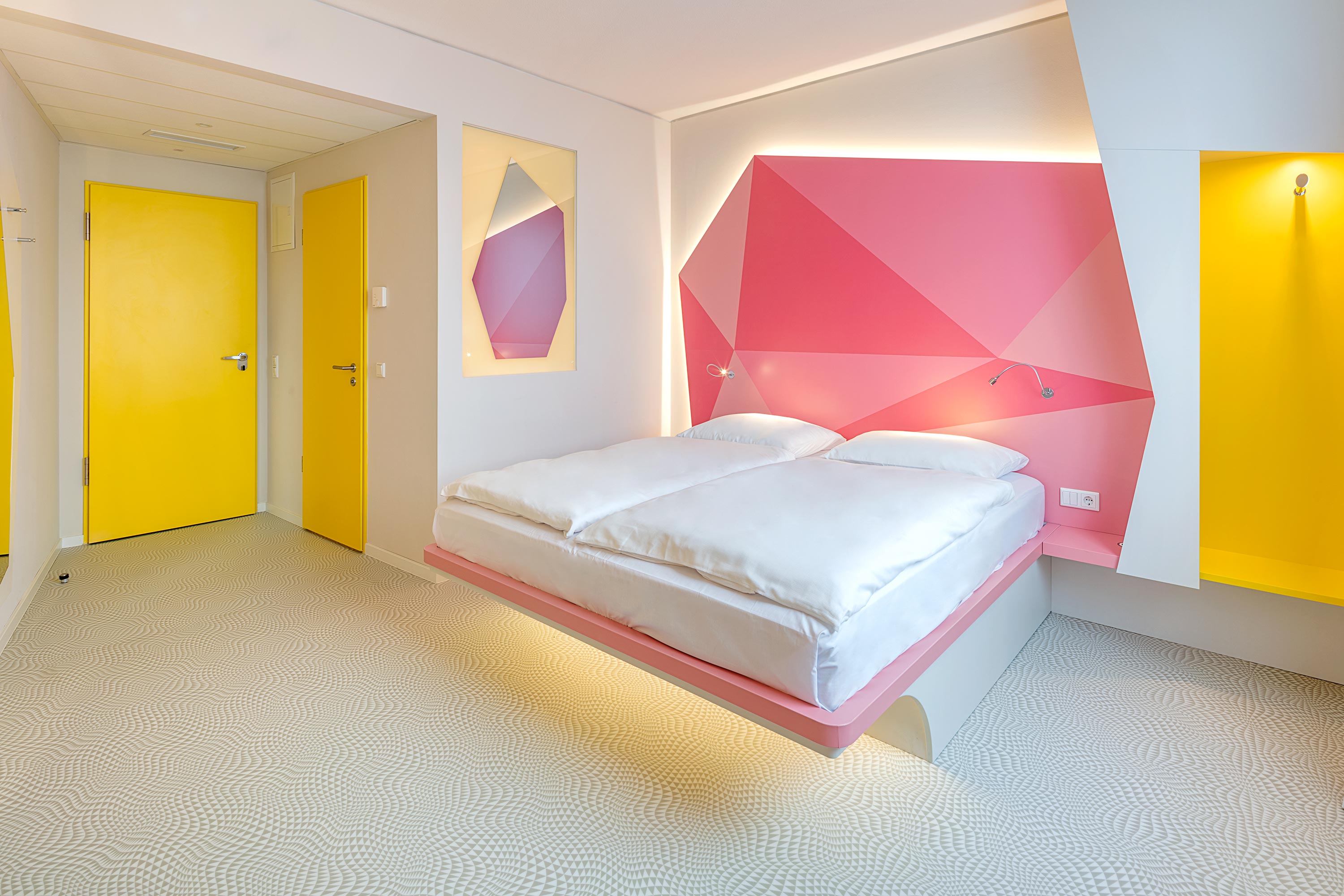 Hotelzimmer mit Doppelbett, rosa Wand und gelber Tür