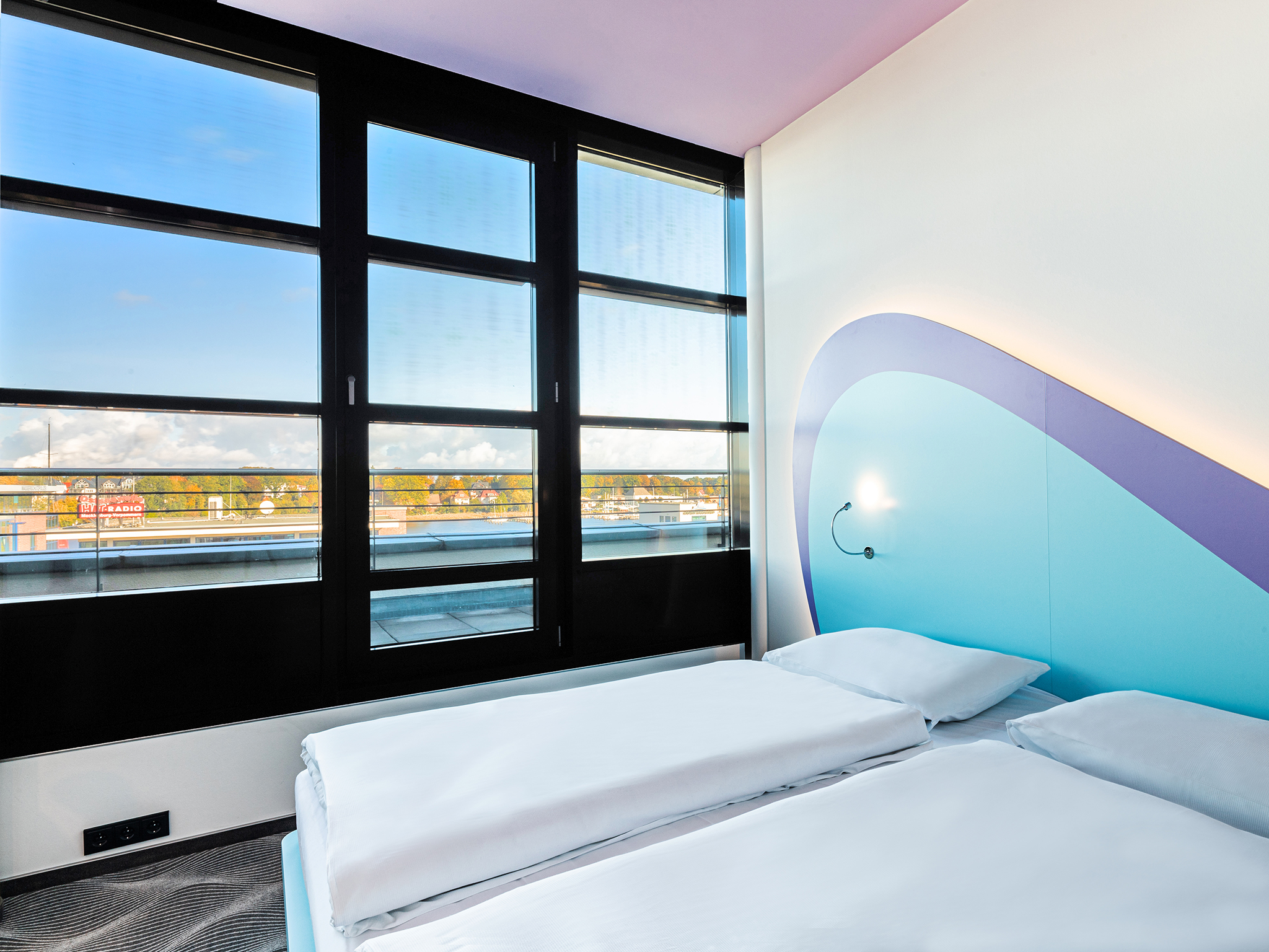 Doppelbett im lichtdurchfluteten Hotelzimmer mit Blick auf die Stadt