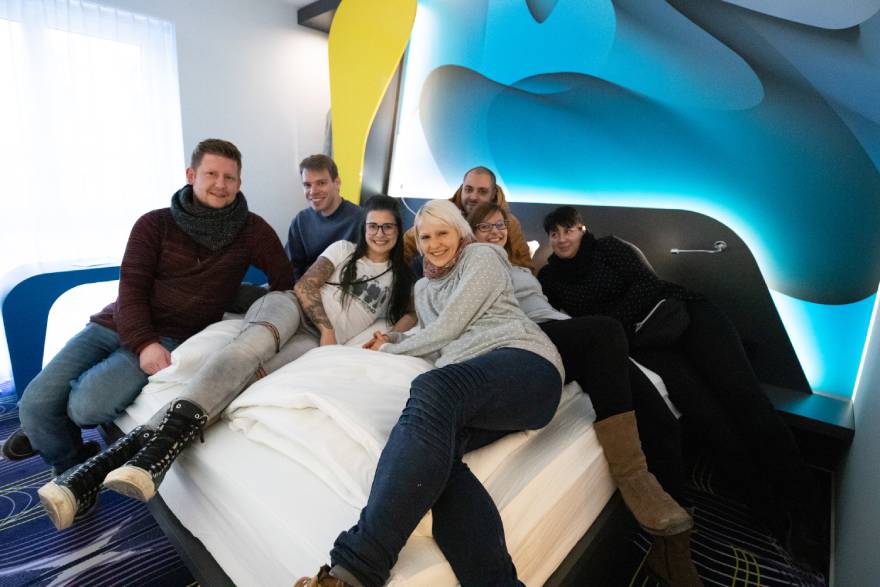 Several employees sitting on a hotel room bed at prizeotel